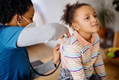 A Black, female doctor uses a stethoscope to check the lungs of a Black, pediatric patient.