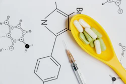 Assortment of Pills, Tablets and Capsules in Yellow Spoon, Syringe on White Background with Chemical Formula.