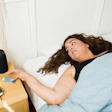 Overweight woman resting in bed next to smart speaker, blue blanket and bedside table