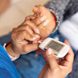 Healthcare professional checking blood glucose meter with patient's hand