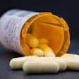 Prescription bottle with orange cap spilling white and yellow capsule pills onto dark surface