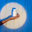 Hand holding white cosmetic bottle against glowing circular light on blue background