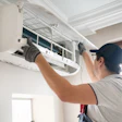 Technician servicing wall-mounted air conditioning unit with open panel access