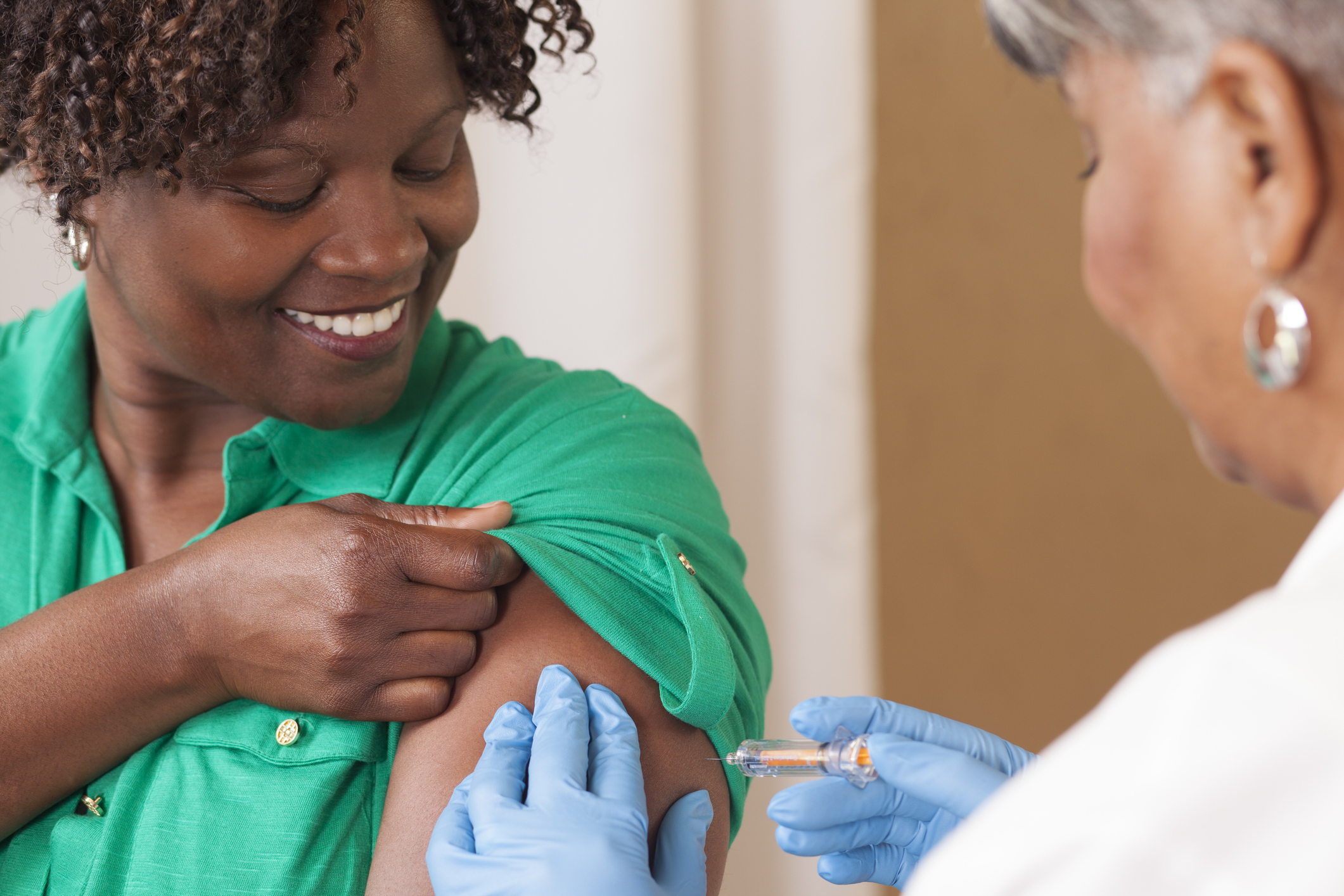 Healthcare worker in green scrubs administering vaccine injection to patient's arm