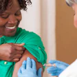 Healthcare worker in green scrubs administering vaccine injection to patient's arm