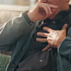 Man sitting on couch holding chest with concerned expression, suggesting health concern or discomfort