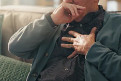 Man sitting on couch holding chest with concerned expression, suggesting health concern or discomfort