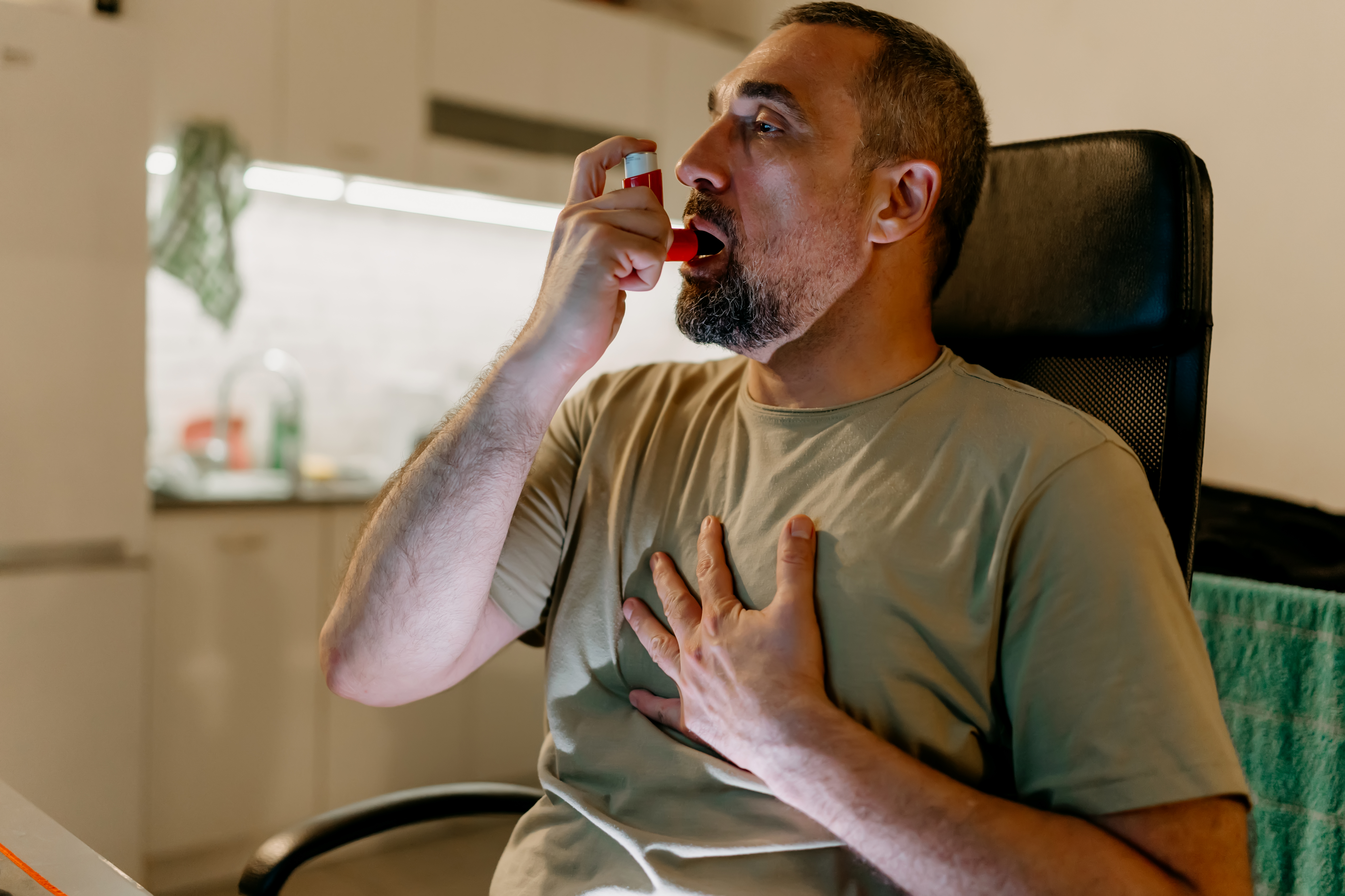 Man in office chair using asthma inhaler during work