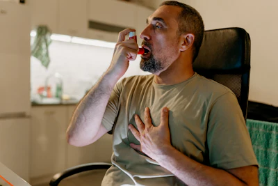 Man in office chair using asthma inhaler during work