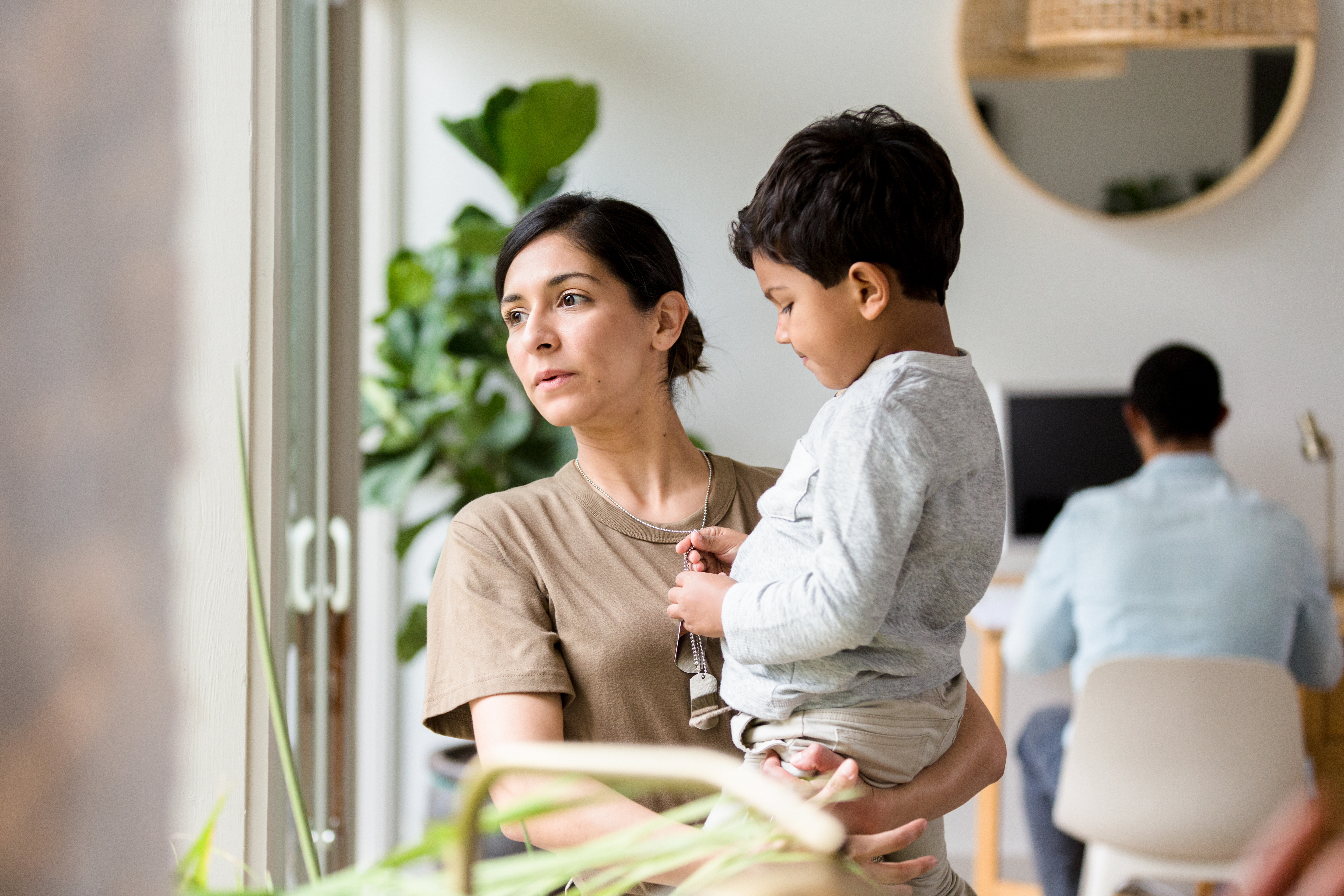 Woman holding toddler in modern office space with colleagues and plants in background