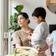 Woman holding toddler in modern office space with colleagues and plants in background