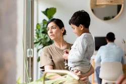 Woman holding toddler in modern office space with colleagues and plants in background