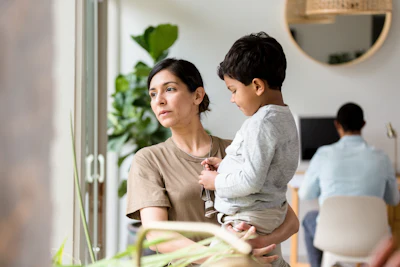 Woman holding toddler in modern office space with colleagues and plants in background