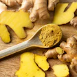 Fresh ginger root and turmeric powder on wooden surface with measuring spoon