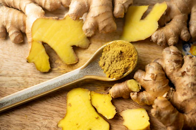 Fresh ginger root and turmeric powder on wooden surface with measuring spoon