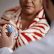 Healthcare provider demonstrating asthma inhaler use to patient wearing red and white striped shirt