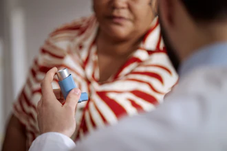 Healthcare provider demonstrating asthma inhaler use to patient wearing red and white striped shirt