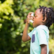 Child using asthma inhaler outdoors with green foliage background