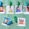 Six printed photos of smiling children clipped to twine with colorful clothespins on a turquoise wooden background