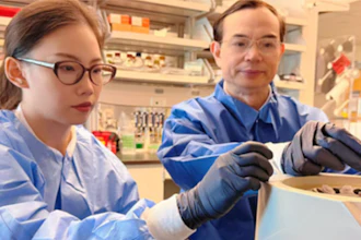 Two researchers in blue lab coats examining samples in a laboratory setting with shelves of scientific equipment and supplies