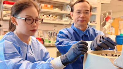 Two researchers in blue lab coats examining samples in a laboratory setting with shelves of scientific equipment and supplies