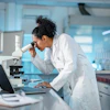 Female scientist using microscope in modern laboratory with laptop and equipment