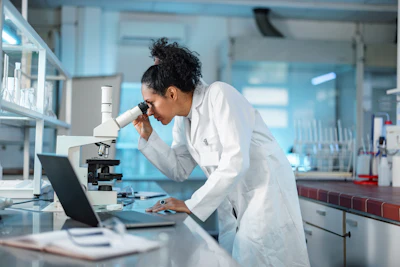 Female scientist using microscope in modern laboratory with laptop and equipment