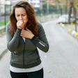 Woman jogging on outdoor path wearing olive green jacket, experiencing chest discomfort while running