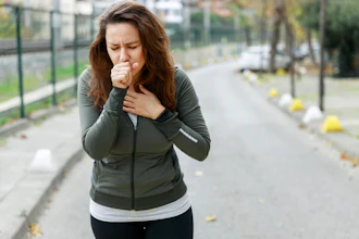 Woman jogging on outdoor path wearing olive green jacket, experiencing chest discomfort while running