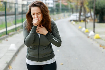 Woman jogging on outdoor path wearing olive green jacket, experiencing chest discomfort while running